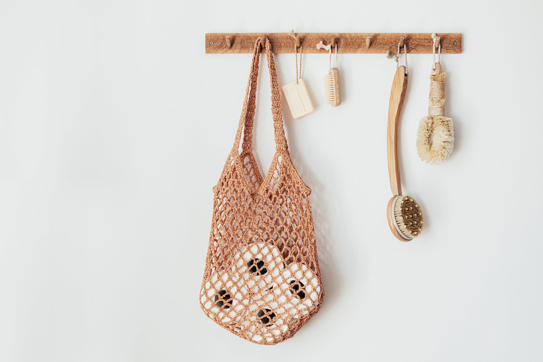 wooden hanger with body brushes and toiletries on white wall